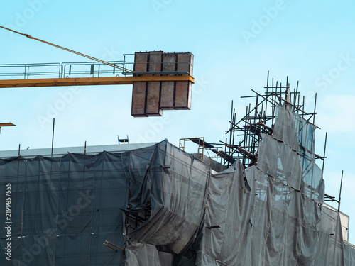 Foto Building under construction wrapped in torn gray safety netting and steel scaffo