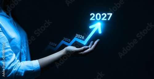 Business growth chart showing upward trend towards 2027 representing future success and financial planning with a hand supporting the rising arrow