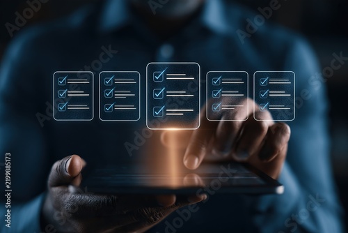 Hands hold a tablet while glowing floating checklist icons hover above, illustrating digital task management and touchscreen workflow.