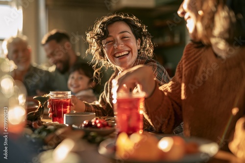 Happy family gathering for dinner meal with laughing woman at table