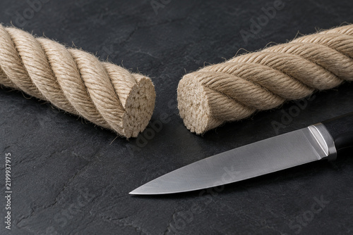 Severed beige rope on dark slate surface with knife, cut rope concept
