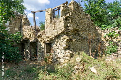 A corner of a ruined house with windows and wooden frames. The masonry is made of light brown stones of varying sizes. A sky with clouds is in the background.