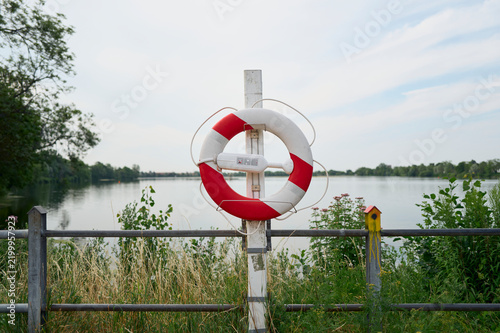 Konstfotografi Red and white life preserver by a calm lake in summer