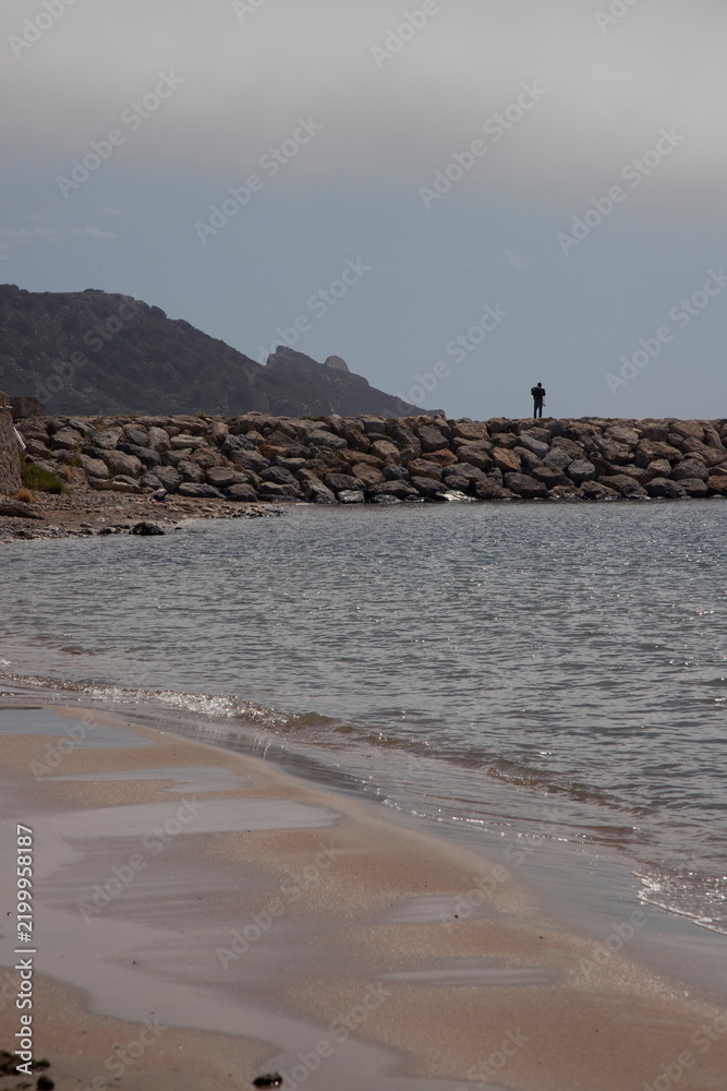 Fototapeta premium Person standing on rocky breakwater viewing calm sea