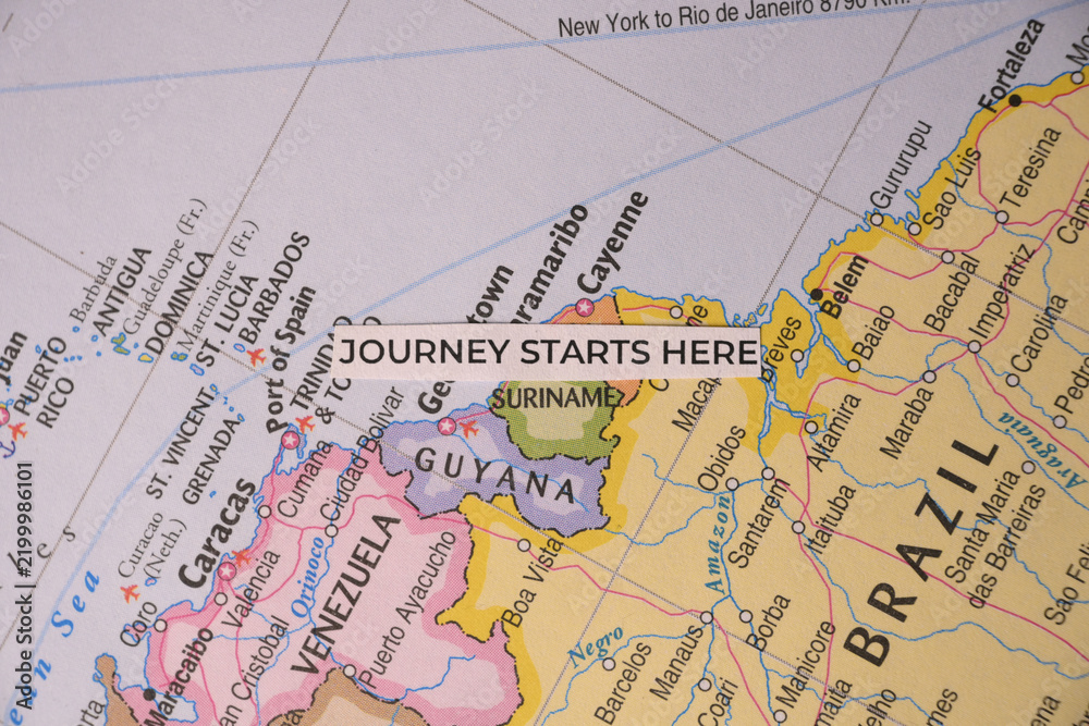 Obraz premium Overhead flat lay of a minimalist paper tag reading journey starts here resting on a physical map of Suriname