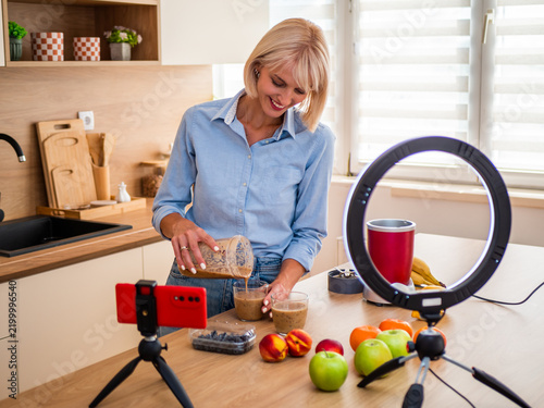 Woman making a homemade smoothie surrounded by colorful fresh fruit in a bright modern kitchen.