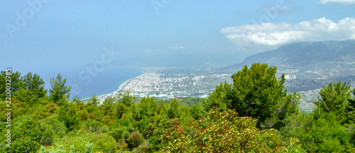 Bild auf Leinwand Alanya, Turkey: ultrawide panoramic view of the Mediterranean coast and coastal city from a green mountain slope, with distant mountains and hazy summer atmosphere