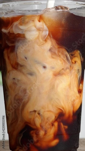 4K footage vertical Close up shot of fresh milk swirling into iced black coffee inside takeaway plastic cup, dynamic fluid motion patterns for iced latte and cold brew coffee menu concept.