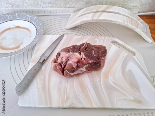 Obraz na płótnie Fresh raw pork meat sliced with knife on white artificial stone cutting board next to ceramic plate and board stand high angle view