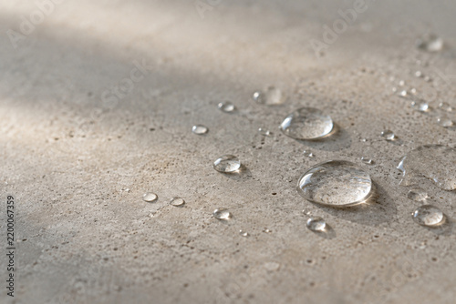 Clear water droplets on neutral stone surface in warm sunlight
