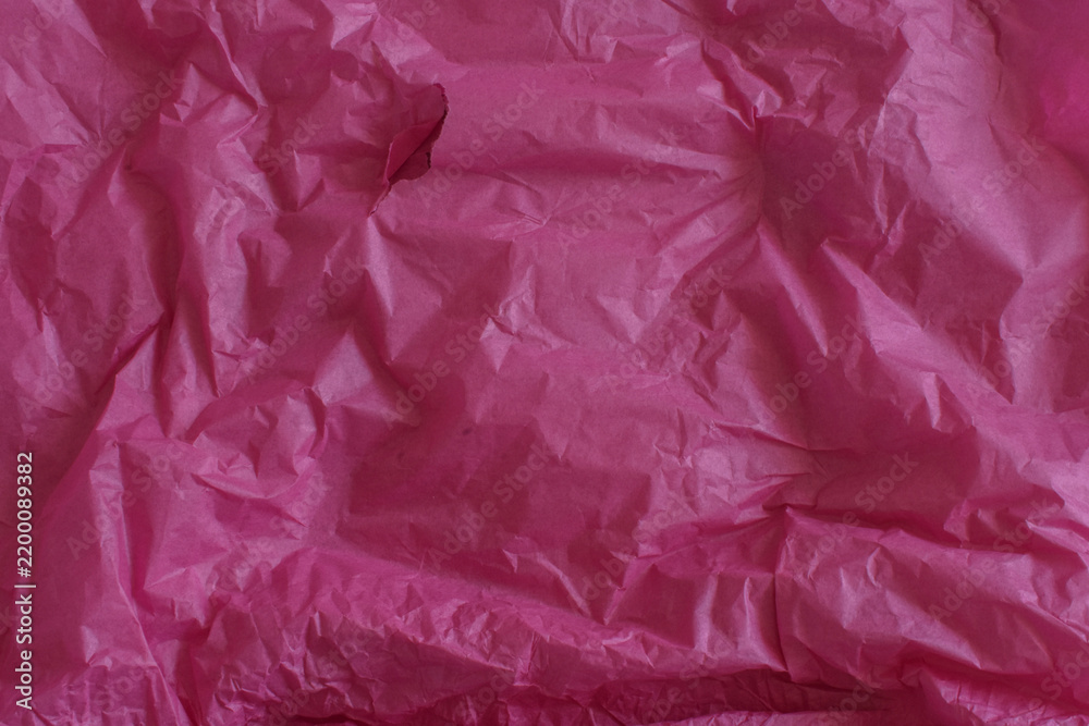 Obraz premium A close-up view of creased and crumpled dark pink wrapping tissue paper, showing detailed wrinkles and folds with a small tear
