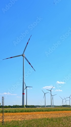 Tall wind turbine standing in green agricultural countryside. Large white wind generator stands in agricultural field with green crops under blue sky on sunny day.