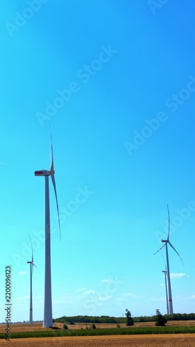 Single wind turbine in open field under blue sky. Tall white wind generator stands in dry agricultural field under blue clear sky on sunny day.