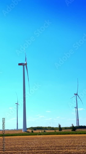 Wind turbines standing in agricultural field under blue sky. Modern white wind generator turbines generate renewable energy in a rural field under direct sunlight.