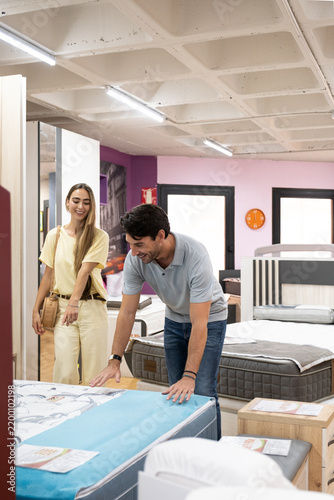 Couple touching and inspecting mattresses in a furniture showroom, deciding on a purchase