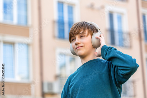 Teenage boy with headphones. Young man with headphones listening to music in the city streets. Portrait child little boy in headphones standing in a summer city and is smiling