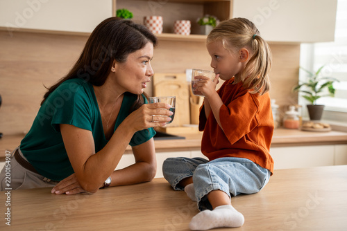 Картината върху платно Mother and daughter staying hydrated together by drinking water in the kitchen