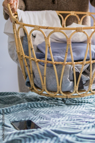 Bild auf Leinwand Woman holds wicker basket filled with clothing items selected for online resale on bed