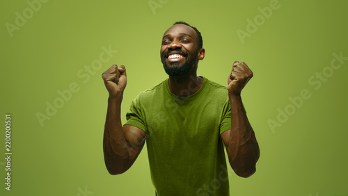Victorious man raises clenched fists in green studio with triumphant excitement. Achievement, winning moment, motivational content concept.