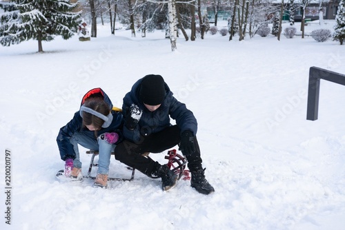 Bild auf Leinwand Winter fun: Two children take a break from sledding in a snowy park, enjoying the quiet moment together
