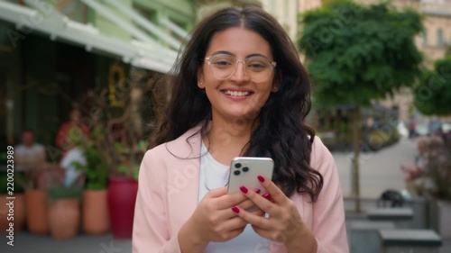 Happy smiling Indian woman holding mobile phone and nodding yes in city street cafe Arabian female girl successful customer user positive client head move okay good reaction approve technology gadget