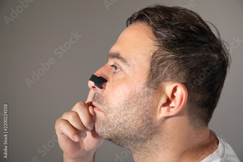 Man applies nasal strip to nose for breathing.