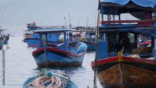 Blue fishing boats drift on calm harbor water with other boats and faint mountains in the background. Peaceful waiting.