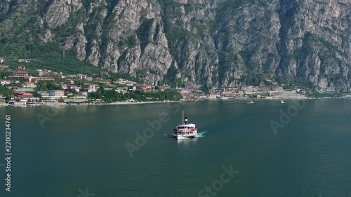 Cinematic rotational 4k zoom drone shot of a large classic motor vessel underway on Lake Garda with dramatic mountains and an Italian village in the background