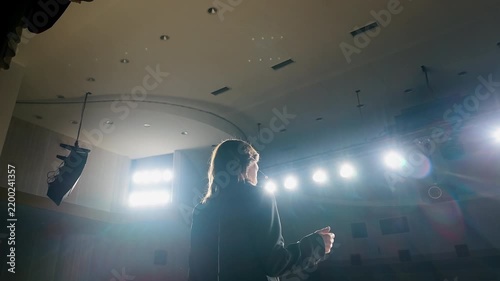 Rear view of a speaker wearing a headset microphone while giving a lecture and presentation on stage. Public speaking, education and professional event concept.
