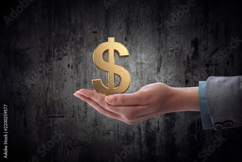 Professional Woman's Hand Holding a 3D Golden Dollar Sign Against Dark Grunge Concrete Background