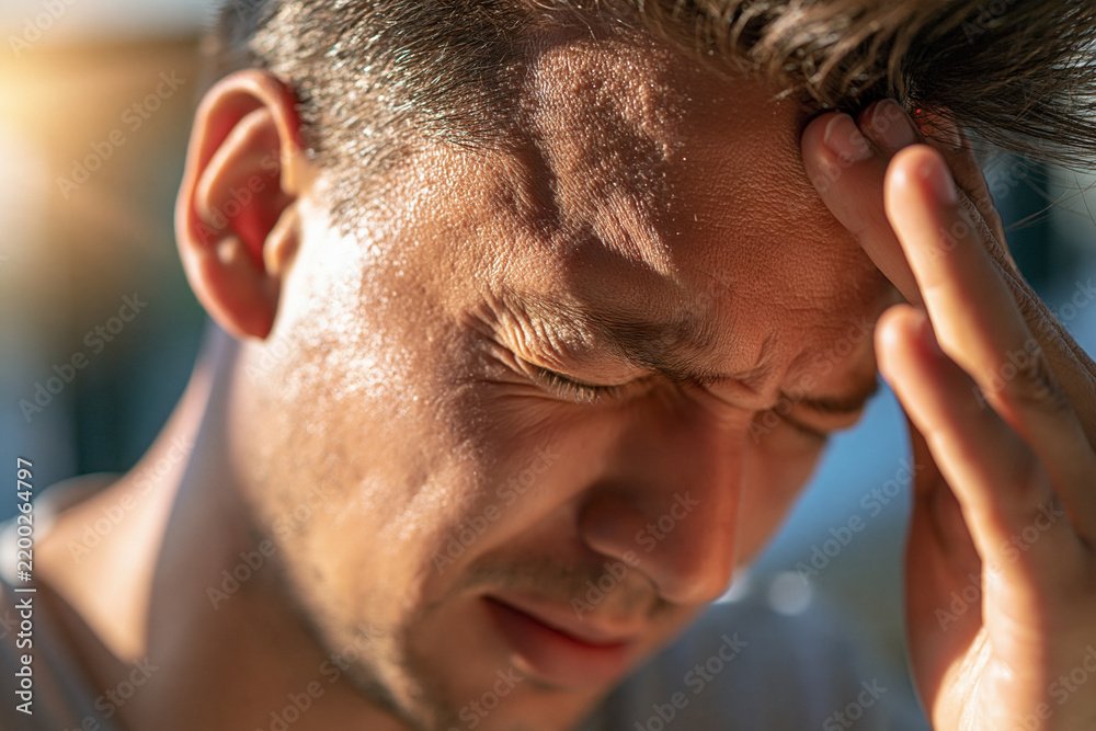 Fototapeta premium Close-up of a faceless adult's hand pressed against the forehead, furrowed skin, eyes out of frame, soft side light, blurred indoor background, severe headache, throbbing head pain