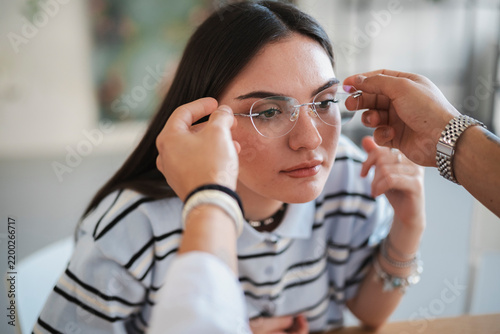 A young woman is trying on a new pair of stylish rimless eyeglasses. An optometrist gently adjusts the frames on her face to ensure a comfortable fit during a consultation.