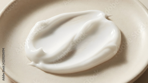 White cosmetic cream smear on a neutral plate, representing skincare, beauty, and smooth texture