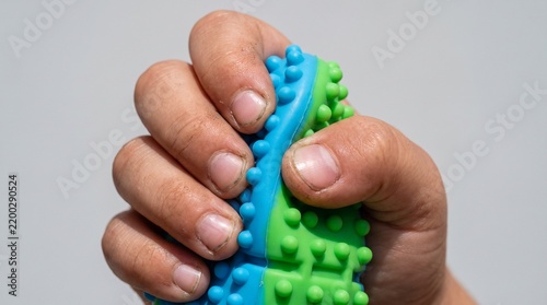 Close up of a hand squeezing a blue and green textured stress ball for relief