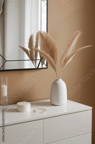 Decorative Vase With Dried Leaves on a White Table Near a Mirror in a Stylish...