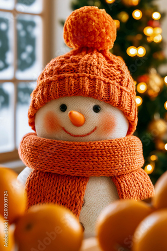 A snowman in an orange hat and scarf against the backdrop of a decorated Christmas tree.