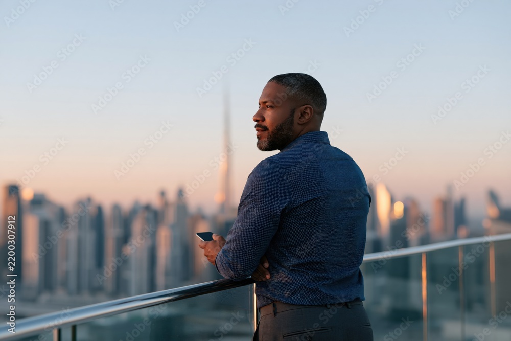 Obraz premium Executive looking over metropolitan skyline from rooftop terrace at sunset for corporate background and banner composition