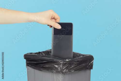 Unplugging from technology, hand throwing black power bank charger into trash bin as concept of digital detox and phone addiction recovery