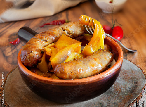 Sausages with yellow peppers in terracotta bowl