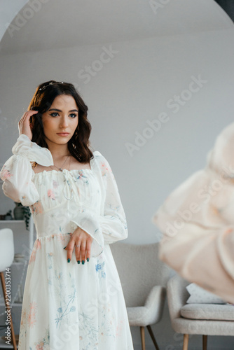 A young woman in a flowing floral dress on a wooden floor beside a large window