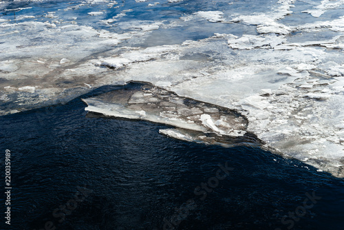 Frozen ice sheets break apart on the surface of a dark, cold river, depicting the beauty and fragility of winter nature.