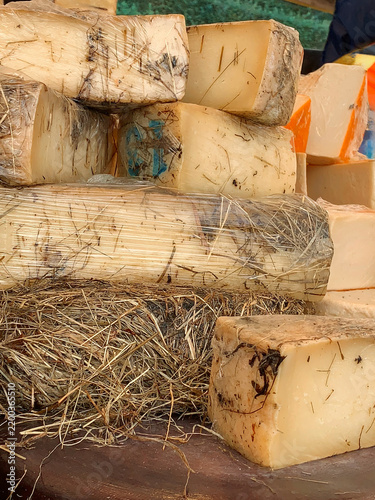 Large blocks of artisan cheese with natural aged rinds are displayed on rustic hay, illustrating traditional dairy production, craftsmanship and authentic market food.