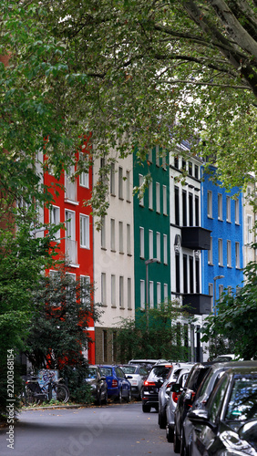 Colorful apartment buildings line a quiet tree-covered residential street with parked cars, illustrating European urban living, neighborhood character and city housing.