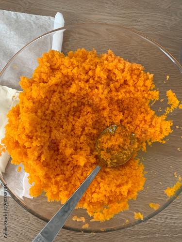 Finely grated fresh pumpkin fills a glass mixing bowl with a spoon on a wooden table, illustrating homemade food preparation, seasonal cooking and healthy ingredients.