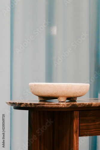 Decorative stone bowl rests on a dark wooden table against softly blurred curtains, creating a calm minimalist interior scene with generous copy space for design use.