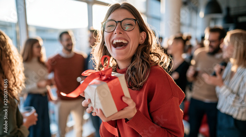 Happy young woman with glasses joyfully holding a gift at a celebration.