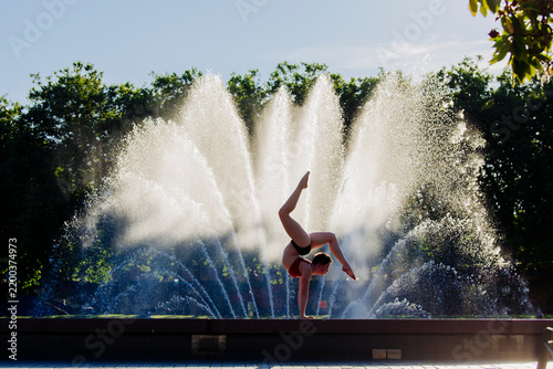 Handstand acrobat balancing in front of water fountain in outdoor park