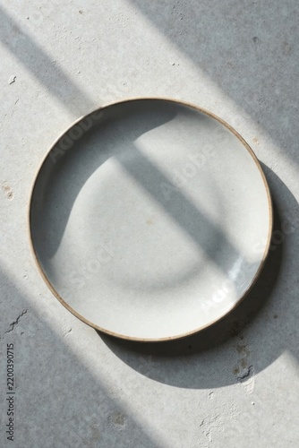 Empty ceramic plate on a textured surface bathed in sunlight