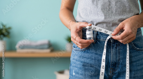 A person holds a vial labeled GLP-1, with a measuring tape around their waist, symbolizing weight loss and health management.