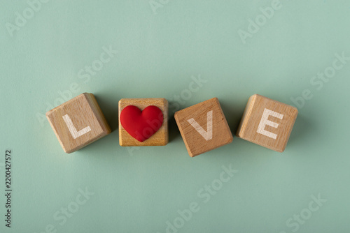 Wooden blocks spelling the word LOVE with a red heart icon replacing the letter O on a light green background. Top view flat lay photography, copy space.